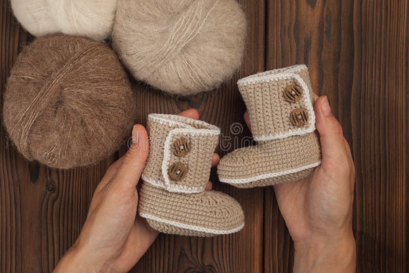 Scarpe di bambino in mani della donna, palle del filato su woodenbackground fotografie stock libere da diritti Scarpe di bambino in mani della donna, palle del filato su woodenbackground fotografie stock libere da diritti