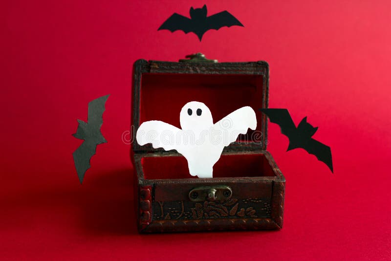 Scary ghost and bats fly out of an old vintage wooden chest on a black background, festive Halloween card