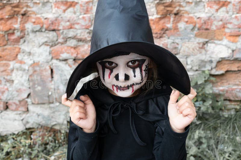 Scary little girl in a witch costume smiles on brick wall background. Happy Halloween. Halloween and day of the dead concept stock photography Scary little girl in a witch costume smiles on brick wall background. Happy Halloween. Halloween and day of the dead concept stock photography