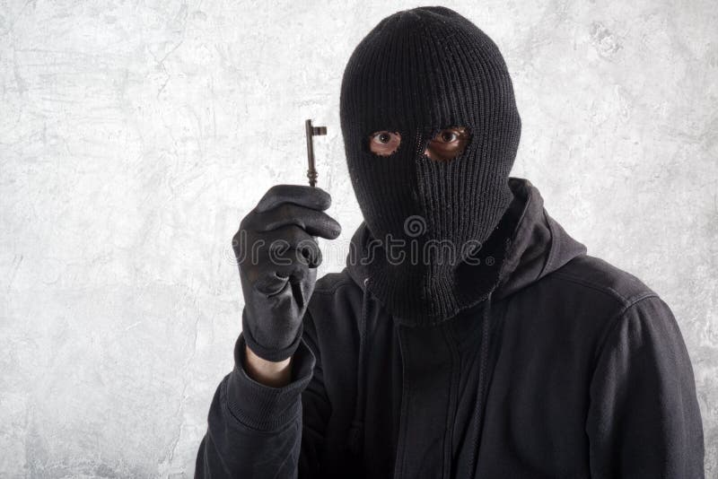 Burglar concept, thief with balaclava caught in front of the grunge concrete wall with an old vintage rusty house key. Burglar concept, thief with balaclava caught in front of the grunge concrete wall with an old vintage rusty house key.