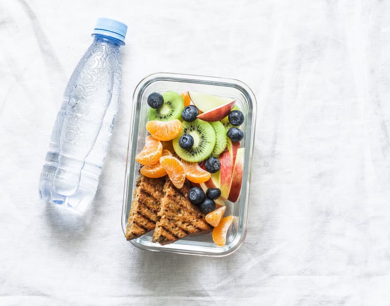 Scatola di pranzo della vitamina dello spuntino sano dell'alimento e bottiglia dolci di acqua pulita su un fondo leggero Pane tos