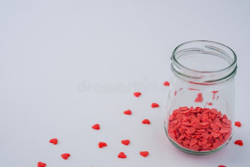 Scatter mini red heart candy from glass jar on white background