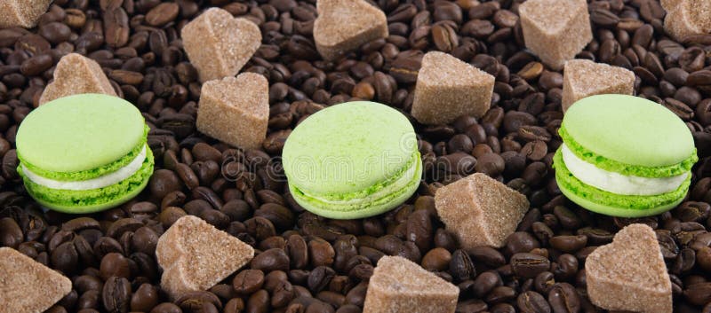 Scattered coffee beans, with three mint macaron cookies, sugar heart, background day of all lovers