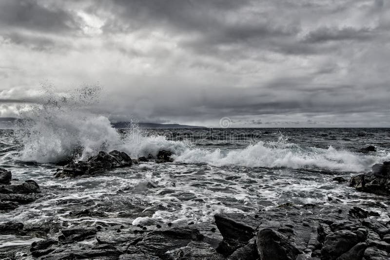 Scatto di grigio di mare ondulato che colpisce la spiaggia rocciosa immagini stock