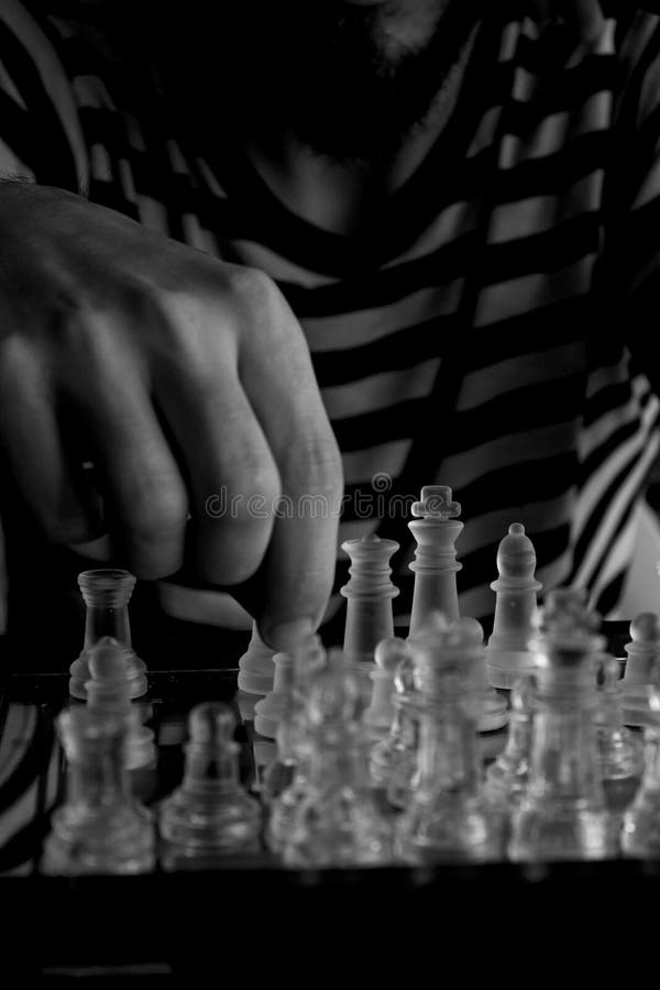Scatto in scala di grigi verticale di un maschio che gioca a scacchi con parti di vetro chiare concetto di strategia immagine stock libera da diritti