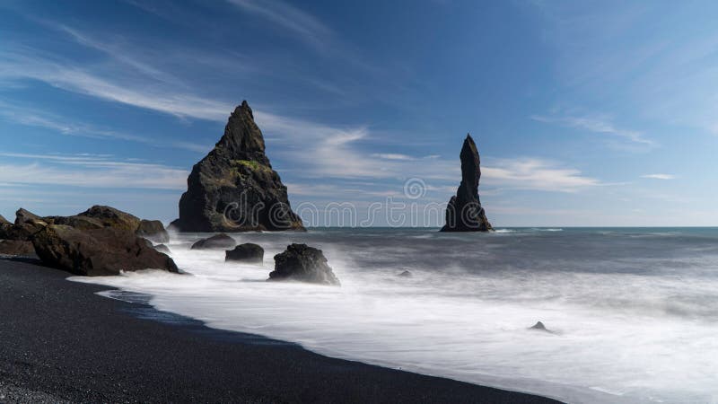 Scen för den svarta stranden i Reynisfjara med höga stenar under blå himmel i Island arkivfoton