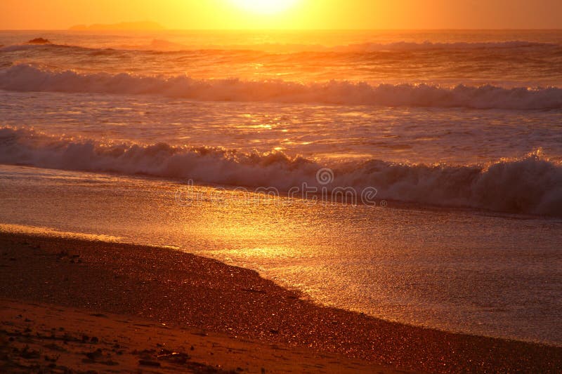 A sunrise over the ocean colors the beach into a golden-orange scenery - at Sapphire Coast, Coffs Harbour, Australia. The island in the background vaguely to see. A sunrise over the ocean colors the beach into a golden-orange scenery - at Sapphire Coast, Coffs Harbour, Australia. The island in the background vaguely to see.