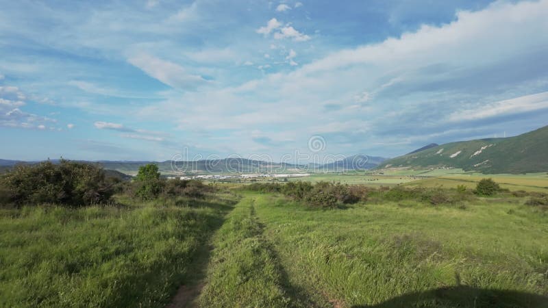 Scenic landscape with a dirt path winding through a grassy field, framed by rolling hills stock footage