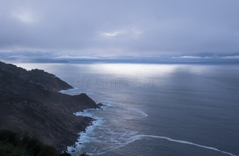 Scenic mysterious mystical seascape landscape with sun rays piercing through clouds sky sunset on atlantic shoreline in deep blue royalty free stock photography
