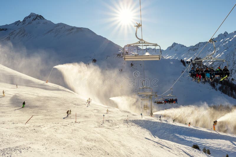 Scenic panoramic view of alpine peaks with ski lift ropeway on hilghland mountain winter resort and snow making machines on bright