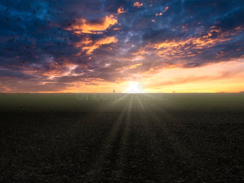 Scenic shot of a beautiful sunrays across the field during sunset under a cloudy sky stock photo