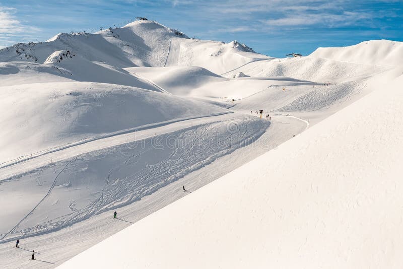 Scenic valley of hilghland alpine mountain winter resort on bright sunny day. Wintersport scene with people enjoy skiing