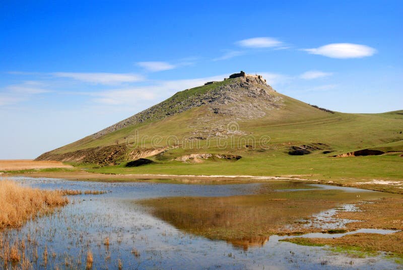 Enisala citadel or Heracleea on top of green hill, lake waters and clear blue sky. Located in Romania. Enisala citadel or Heracleea on top of green hill, lake waters and clear blue sky. Located in Romania.