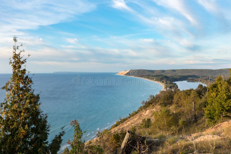 Scenic overlook on the Empire Bluffs Trail overlooks Lake Michigan, Sleeping Bear Dunes National Lakeshore, South Manitou Island, and North Bar Lake, under a blue sky with white clouds. Scenic overlook on the Empire Bluffs Trail overlooks Lake Michigan, Sleeping Bear Dunes National Lakeshore, South Manitou Island, and North Bar Lake, under a blue sky with white clouds.