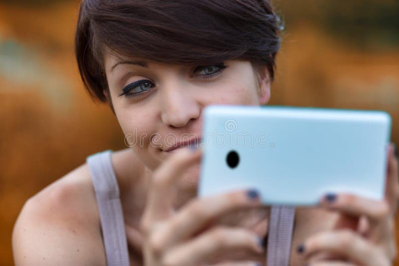 Sceptical young woman looking at her mobile phone with a wry smile and expression of disbelief in a close up cropped portrait. Sceptical young woman looking at her mobile phone with a wry smile and expression of disbelief in a close up cropped portrait