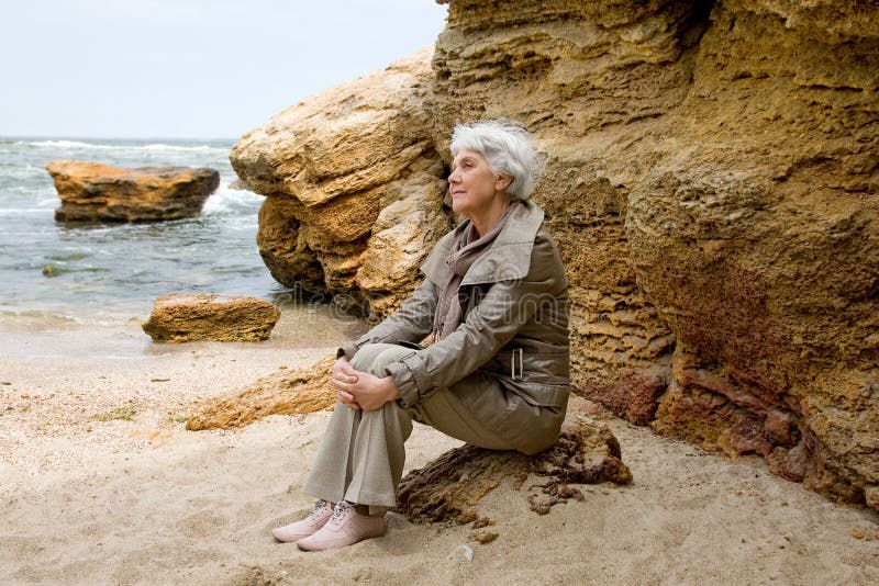 Schöne nette ältere Frau, die auf dem Strandmeer und -blicken in den Abstan...