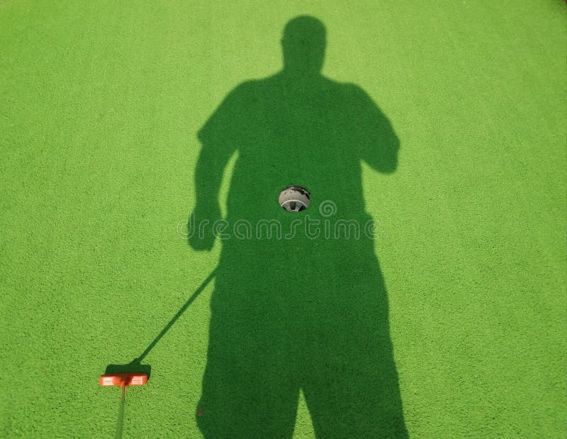 Schaduw van de mens met golfputter op een miniatuur golfgat stock foto Schaduw van de mens met golfputter op een miniatuur golfgat stock foto