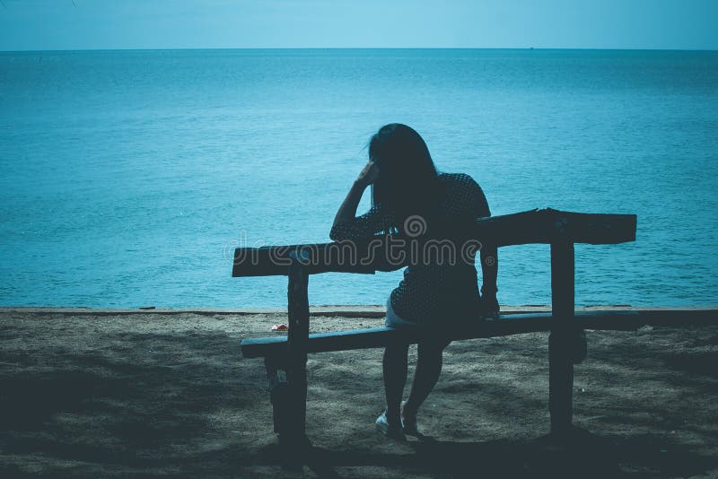 Schattenbild der einsamen Frau sitzend auf Holzbank auf dem Strand und zum blauen Meer schauend lizenzfreie stockfotografie