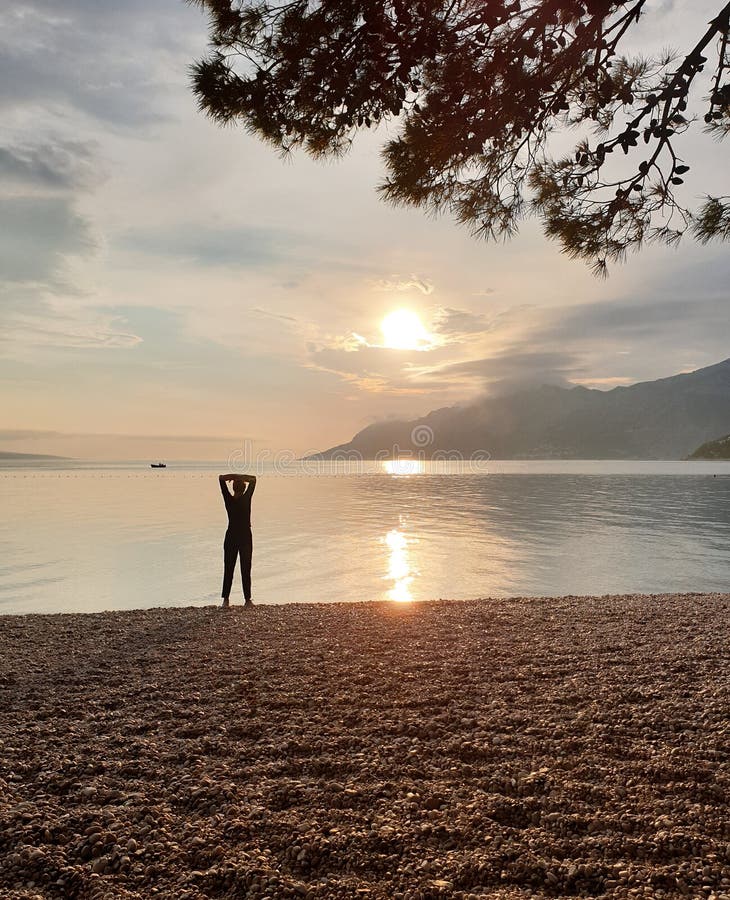 Schattenbild einer schlanken Frau, die den Sonnenuntergang betrachtet, der auf der Küste steht Genießen entspannenden Sommerferie lizenzfreies stockbild Schattenbild einer schlanken Frau, die den Sonnenuntergang betrachtet, der auf der Küste steht Genießen entspannenden Sommerferie lizenzfreies stockbild