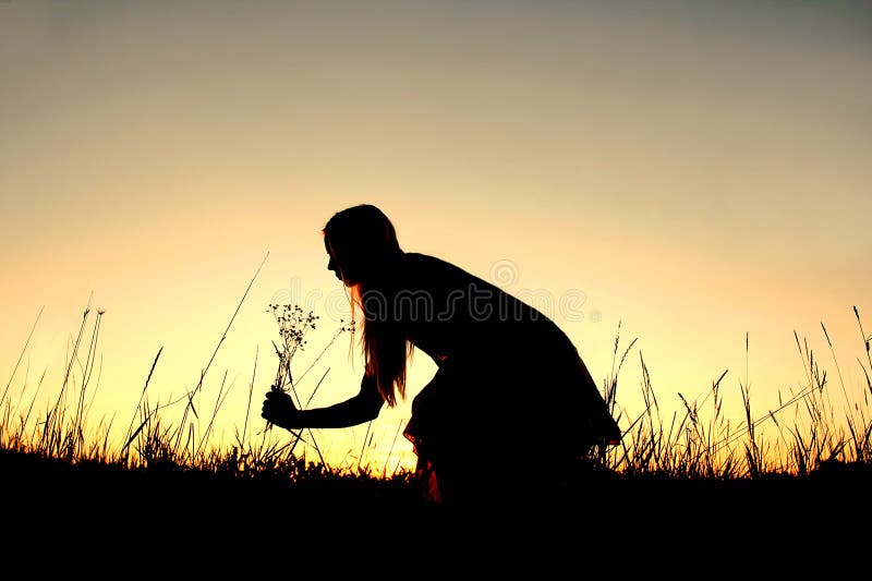 A silhouette of a happy girl outside picking wild flowers in the meadow at sunset. A silhouette of a happy girl outside picking wild flowers in the meadow at sunset.