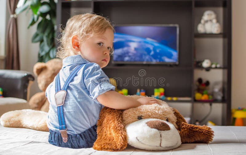 Cute baby boy and his dog plush toy watching TV sitting on a couch in the living room at home. Cute baby boy and his dog plush toy watching TV sitting on a couch in the living room at home.