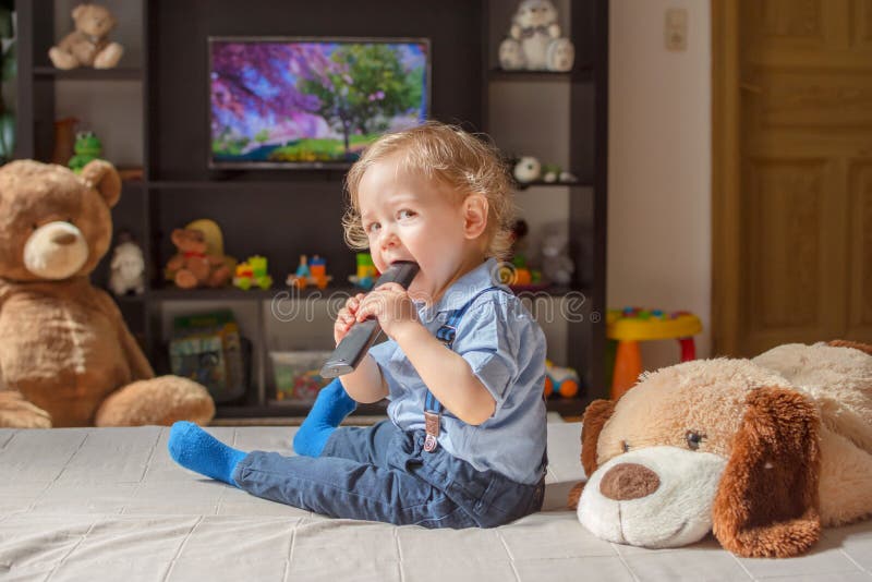 Cute baby boy and his dog plush toy watching TV sitting on a couch in the living room at home. Cute baby boy and his dog plush toy watching TV sitting on a couch in the living room at home.