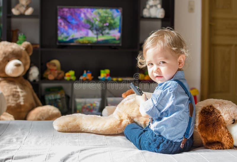 Cute baby boy and his dog plush toy watching TV sitting on a couch in the living room at home. Cute baby boy and his dog plush toy watching TV sitting on a couch in the living room at home.