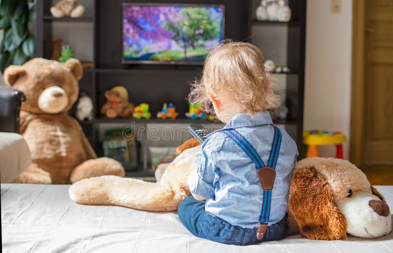 Cute baby boy and his dog plush toy watching TV sitting on a couch in the living room at home. Cute baby boy and his dog plush toy watching TV sitting on a couch in the living room at home.