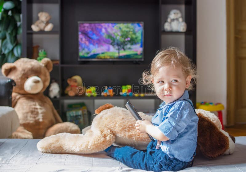 Cute baby boy and his dog plush toy watching TV sitting on a couch in the living room at home. Cute baby boy and his dog plush toy watching TV sitting on a couch in the living room at home.