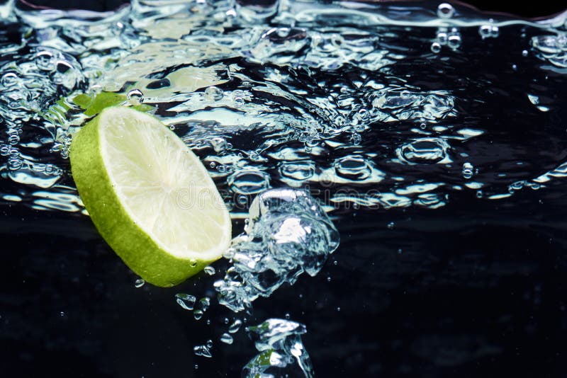 Scheibe des Kalkes (Zitrone) fallend in Wasser lizenzfreie stockbilder