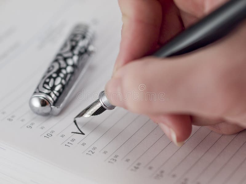 Woman hand holding pen and making mark on a day planner at 11am. Woman hand holding pen and making mark on a day planner at 11am.