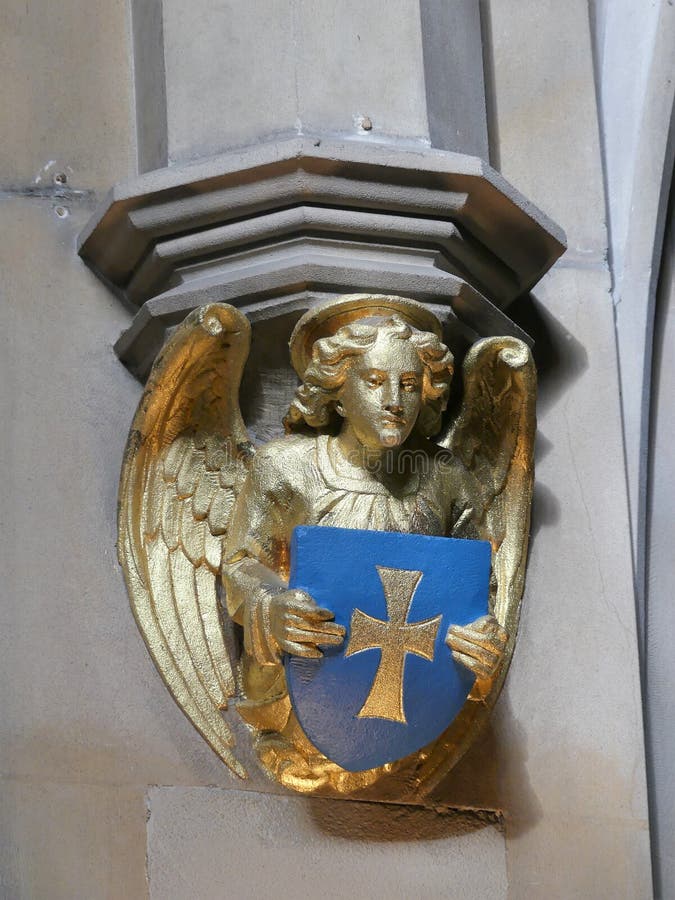 Schermo dorato della tenuta della scultura di angelo della parete della chiesa e guardare giù immagini stock Schermo dorato della tenuta della scultura di angelo della parete della chiesa e guardare giù immagini stock