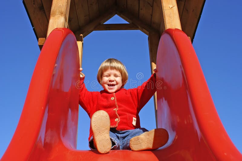 Two and a half year old girl preparing to come down on a red slide. Two and a half year old girl preparing to come down on a red slide