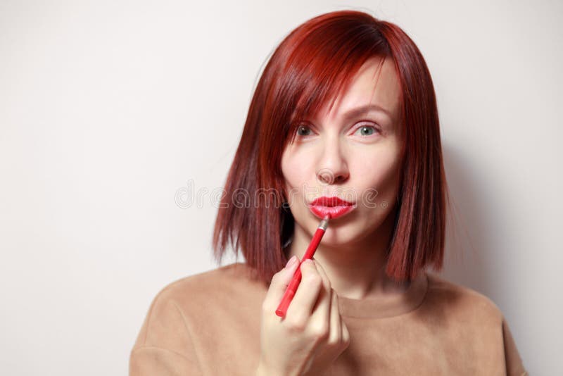 Schildert het het roodharige mooie meisje van het close-upportret haar lippen met rode potloodlippenstift De conceptenschool van stock afbeelding Schildert het het roodharige mooie meisje van het close-upportret haar lippen met rode potloodlippenstift De conceptenschool van stock afbeelding