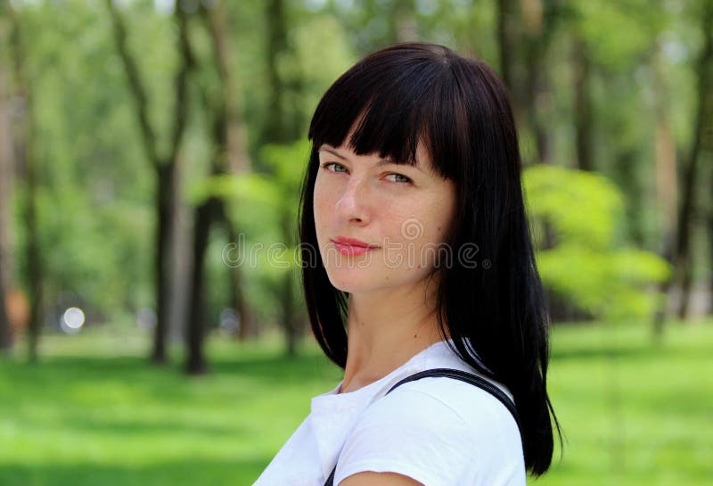 Schitterend jong vrouwenmodel met donker haar die de camera bekijken, die in het park in een witte T-shirt stellen royalty-vrije stock foto's Schitterend jong vrouwenmodel met donker haar die de camera bekijken, die in het park in een witte T-shirt stellen royalty-vrije stock foto's