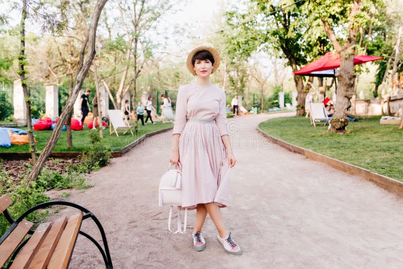 Schitterend meisje in een trendy hoed met benen doorkruist in de buurt van de houten bank in het park Charterende jonge vrouw met royalty-vrije stock fotografie Schitterend meisje in een trendy hoed met benen doorkruist in de buurt van de houten bank in het park Charterende jonge vrouw met royalty-vrije stock fotografie