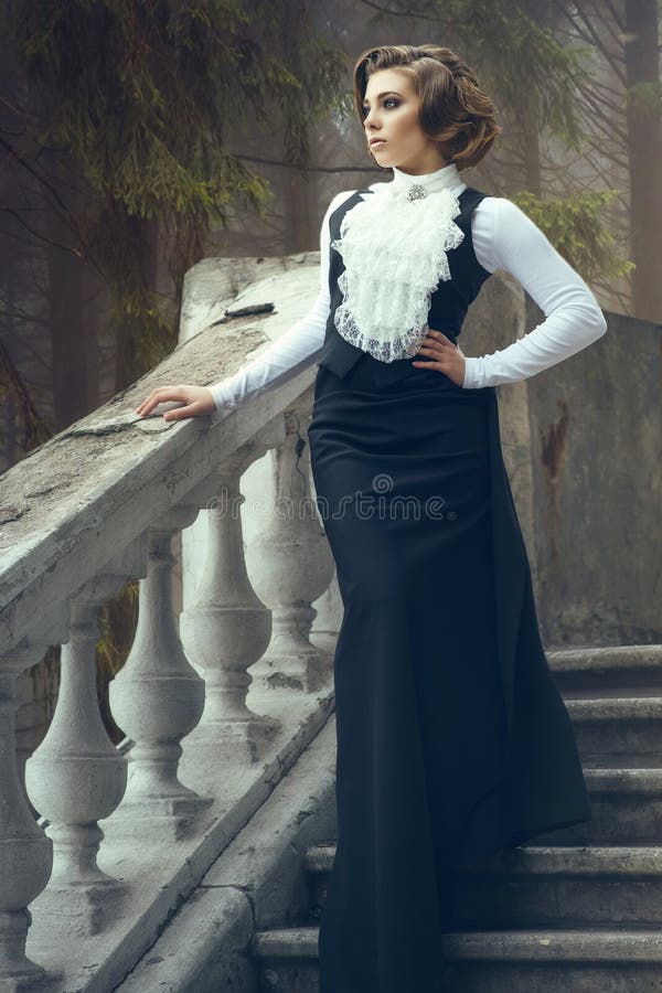 Schitterende vrouw met elegant kapsel die ouderwetse toga dragen die zich op oud de stappen op haar kasteel bevinden stock afbeelding Schitterende vrouw met elegant kapsel die ouderwetse toga dragen die zich op oud de stappen op haar kasteel bevinden stock afbeelding