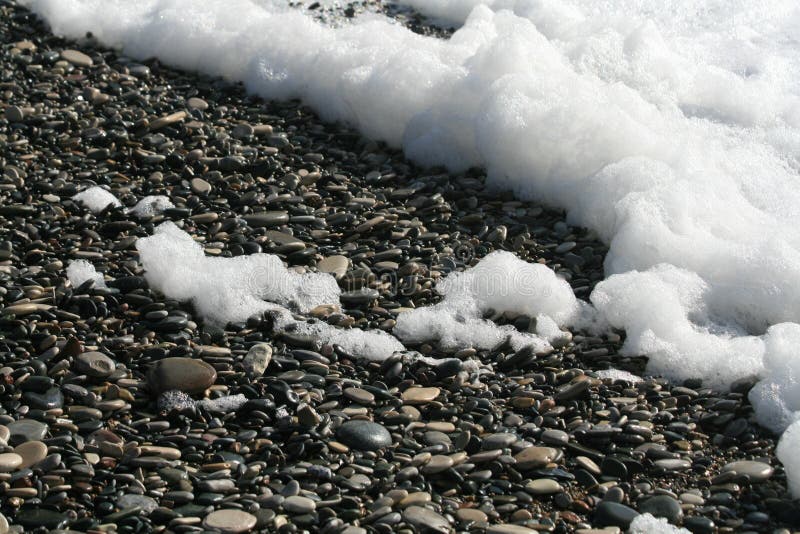 Schiuma spessa del mare su una spiaggia dell'assicella fotografia stock Schiuma spessa del mare su una spiaggia dell'assicella fotografia stock