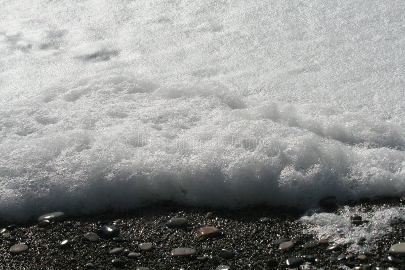 Schiuma spessa del mare su una spiaggia dell'assicella immagine stock libera da diritti Schiuma spessa del mare su una spiaggia dell'assicella immagine stock libera da diritti