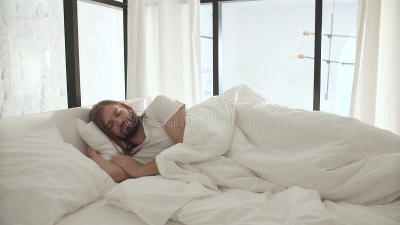 Schlafender Mann im Bett mit weißen Leinen am hellen Schlafzimmer stock video footage