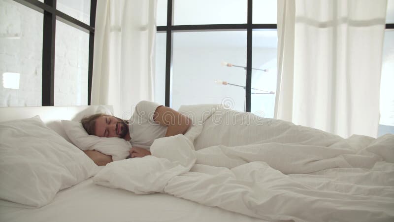 Schlafender Mann im Bett mit weißen Leinen am hellen Schlafzimmer stock footage