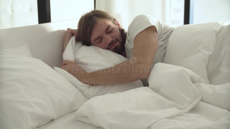 Schlafender Mann im Bett mit weißen Leinen am hellen Schlafzimmer stock video