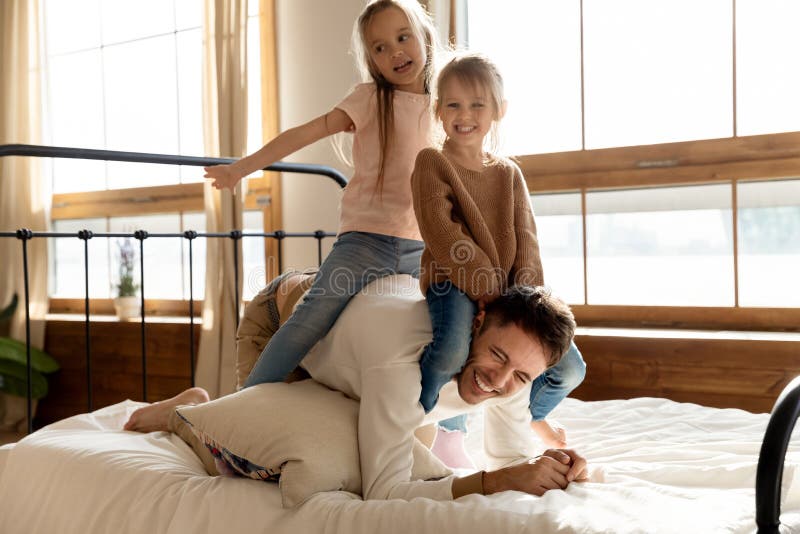 In Schlafzimmer zwei spielen kleine heitre Töchter mit Vati stockfotografie