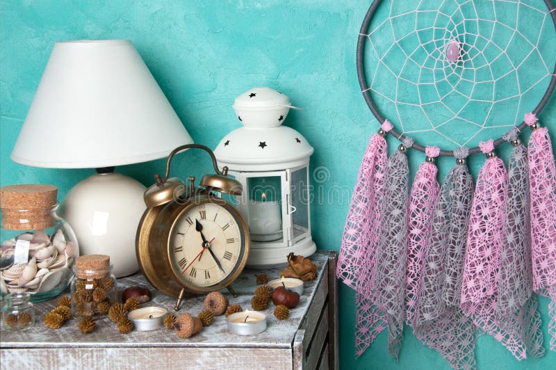 Pink gray dream catcher , alarm clock and aroma candles in bedroom interior on aquamarine textured background. Bedroom decor. Pink gray dream catcher , alarm clock and aroma candles in bedroom interior on aquamarine textured background. Bedroom decor.