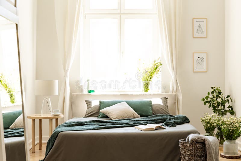 Bedroom interior in nature colors with big bed, gray and green linen and pillows, fresh meadow flowers and a sunny window in the background. Real photo. concept. Bedroom interior in nature colors with big bed, gray and green linen and pillows, fresh meadow flowers and a sunny window in the background. Real photo. concept