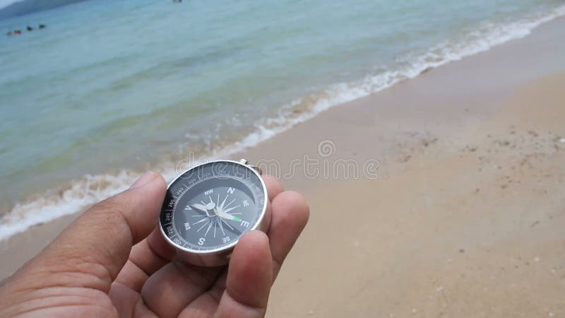 Schließen Sie herauf die Schusshand von mand einen Kompass auf dem Sandstrand mit Naturmeer halten und wickeln Sie umgebenden Ton