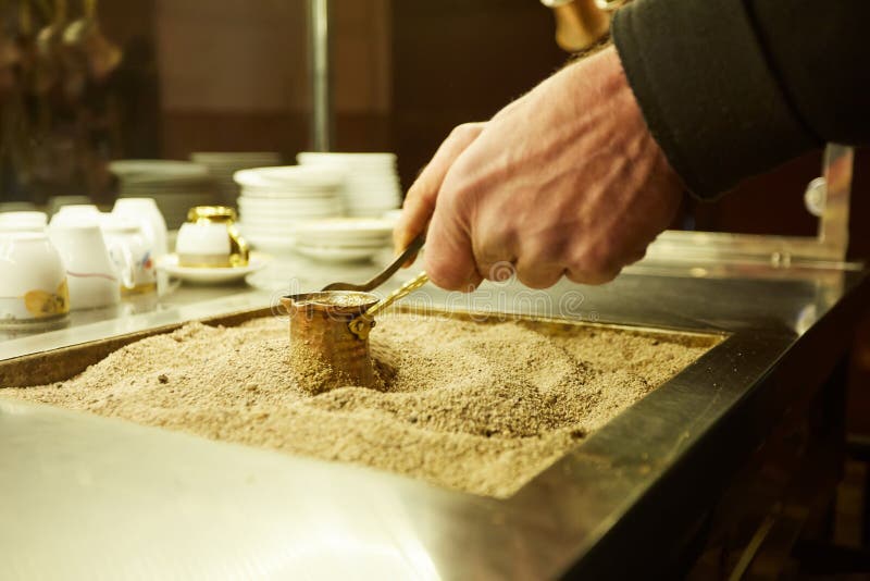 Schließen Sie herauf Hände eines Mannes, der türkischen Kaffee auf heißem goldenem Sand kocht lizenzfreies stockfoto Schließen Sie herauf Hände eines Mannes, der türkischen Kaffee auf heißem goldenem Sand kocht lizenzfreies stockfoto
