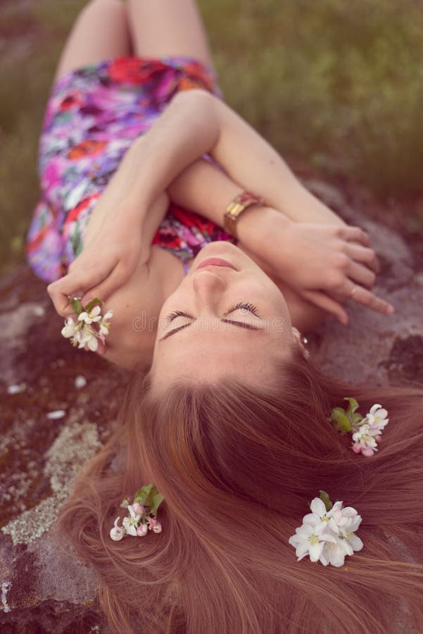 Schließen Sie herauf Porträt der schönen blonden jungen Frau, die auf Stein mit Blumen in ihren schließend Augen des Haares legt, lizenzfreie stockbilder Schließen Sie herauf Porträt der schönen blonden jungen Frau, die auf Stein mit Blumen in ihren schließend Augen des Haares legt, lizenzfreie stockbilder