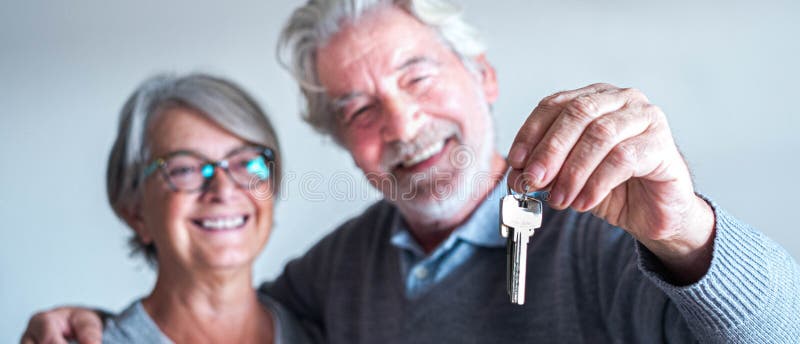 Close up and portrait of two seniors or mature people buying a new house or car or some property - independent lifesyle and concept - pensioner man holding two keys in his hand with his wife looking at it. Close up and portrait of two seniors or mature people buying a new house or car or some property - independent lifesyle and concept - pensioner man holding two keys in his hand with his wife looking at it