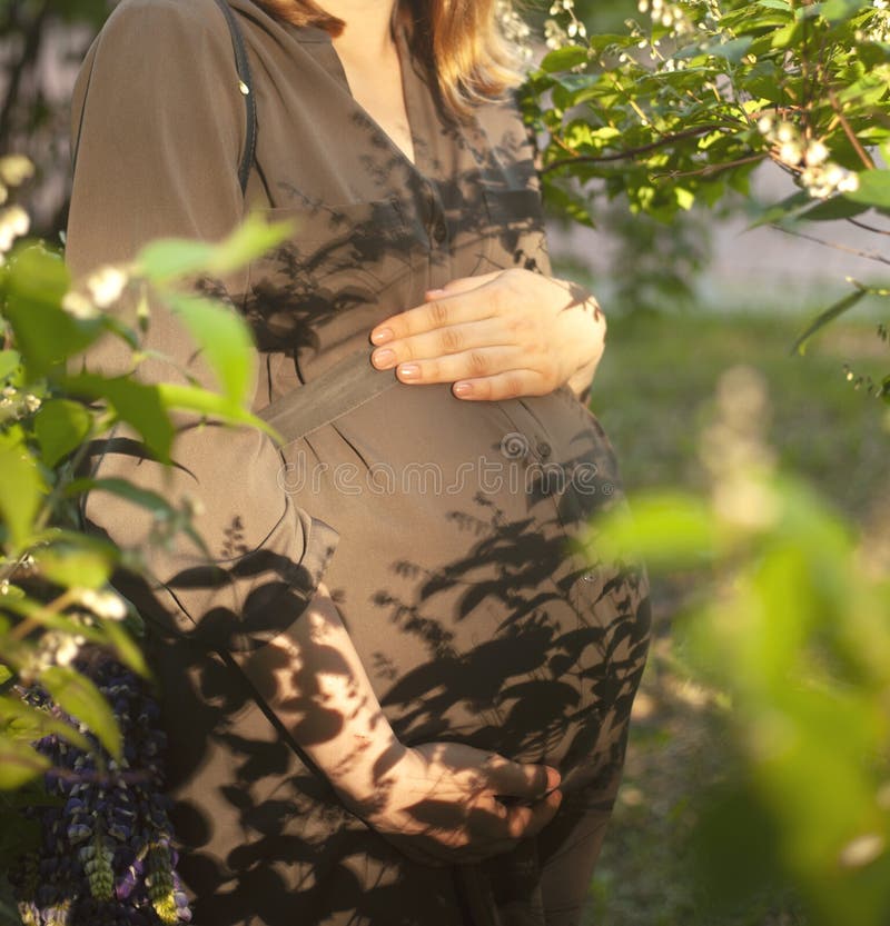 Schließen Sie oben vom Bauch einer schwangeren Frau in einem Sommerpark stockbilder Schließen Sie oben vom Bauch einer schwangeren Frau in einem Sommerpark stockbilder